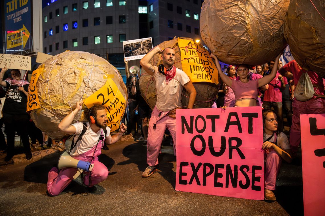 Protestirende mit großen Kugeln aus Karton und rosa farbenen Schildern protestieren gegen die israelische Regierung.