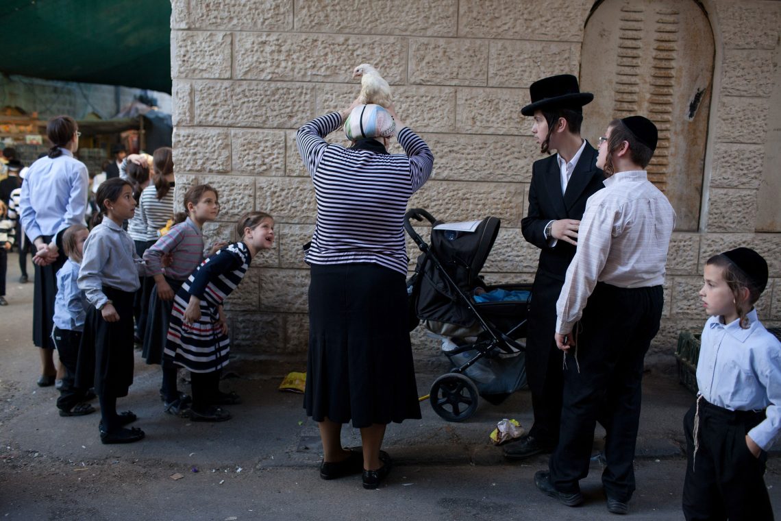 Eine Gruppe ultra-orthodoxer Juden bei einem Kaparot-Ritual. Kinder schauen neugierig zu. Eine Straßenszene in Jerusalem. Das Bild ist Teil eines Beitrags über die Regierung in Israel.