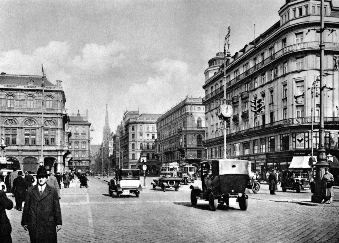 Die Kärntner Straße in Wien circa 1920. Einige Autos fahren Richtung Café Sacher und Stephansplatz, linker Hand die Oper. Einige Menschen gehen zu Fuß.
