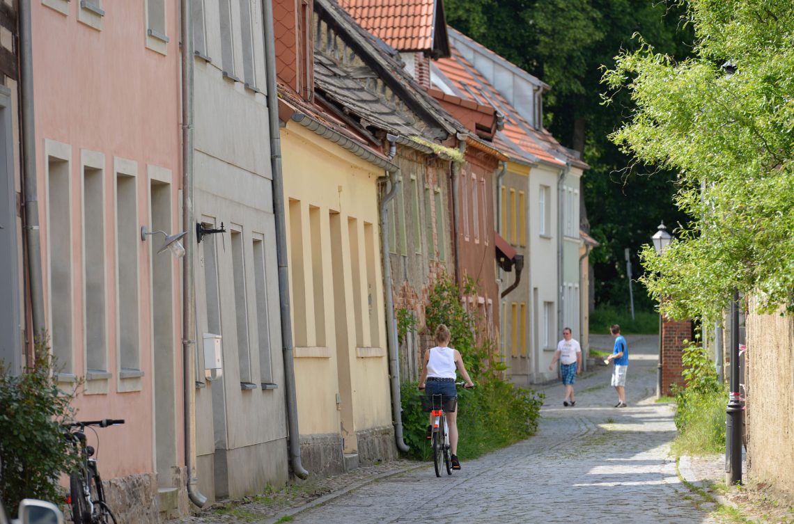 Foto einer mit Kopfstein gepflasterten Straße, die von alten Häusern gesäumt ist. Der Ort, Bad Belzig, ist ein Beispiel für die neue Landlust von eigentlich urbanen Menschen, die alte Dörfer neu beleben.