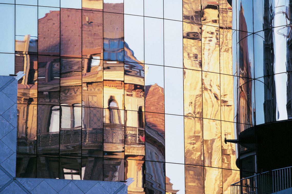Spiegelung von Stephandom und weiteren alten Gebäuden in der Fassade des Haas-Hauses in Wien. Das Bild ist Teil eines Beitrags über Stadtflucht und das Leben in der Stadt im Gegensatz zum Land – vor allem in ökonomischer Hinsicht.