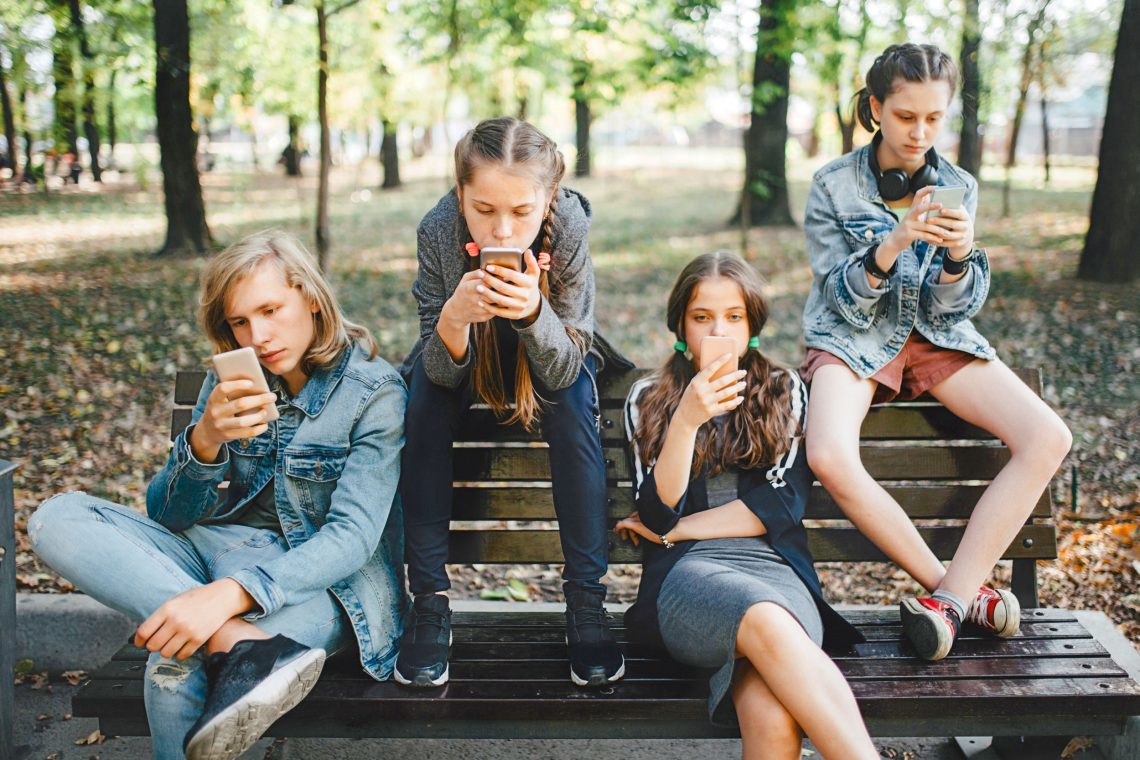 Foto von Jugendlichen, die auf einer Bank sitzen und auf Smartphones etwas lesen. Das Bild ist Teil eines Beitrags über gute Nachrichten und die Rolle der Medien.
