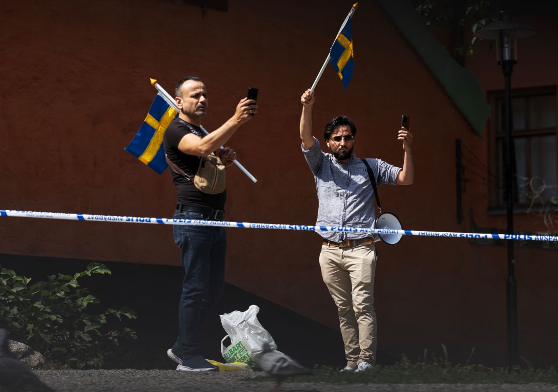 Zwei Männer schwenken schwedische Fahnen und filmen sich mit ihren Mobiltelefonen.