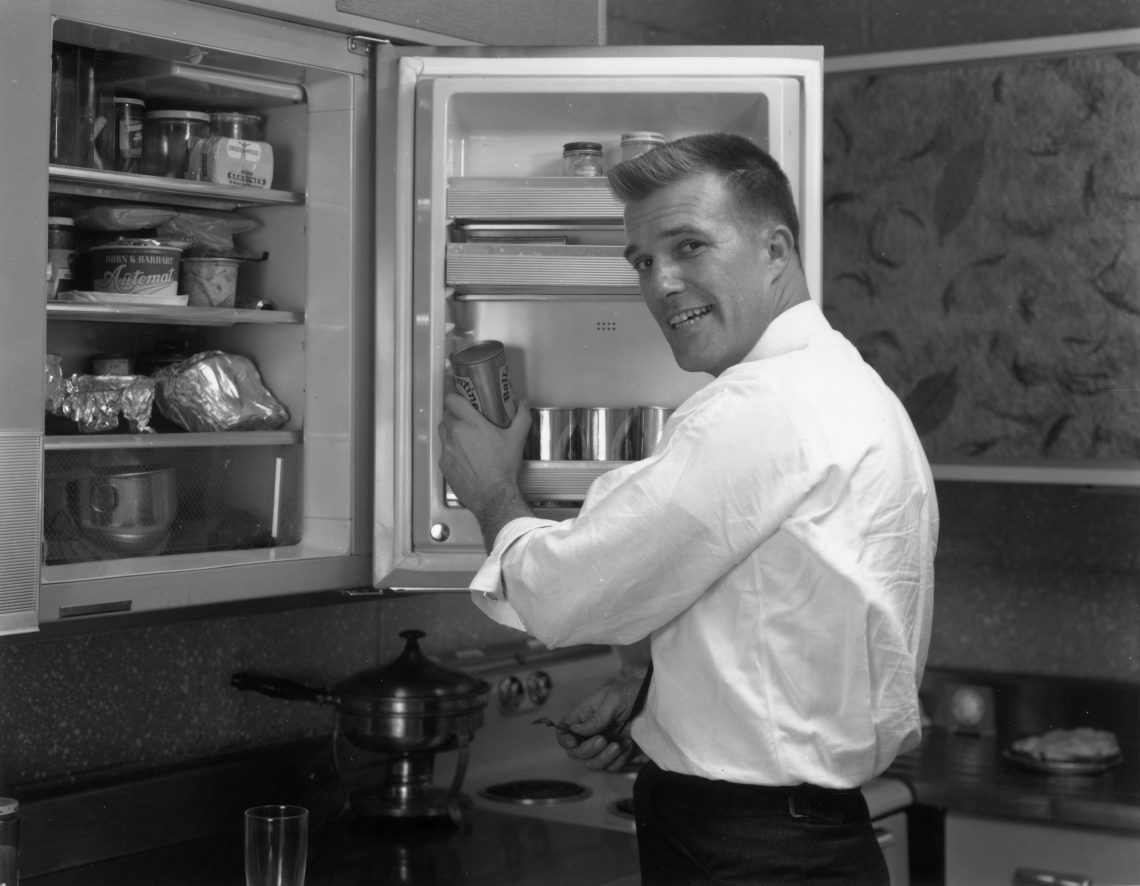 Foto eines Mannes vor einem geöffneten Kühlschrank, der lächelnd über seine Schulter in die Kamera blickt. Das Bild ist Teil eines Textes über Zuversicht.