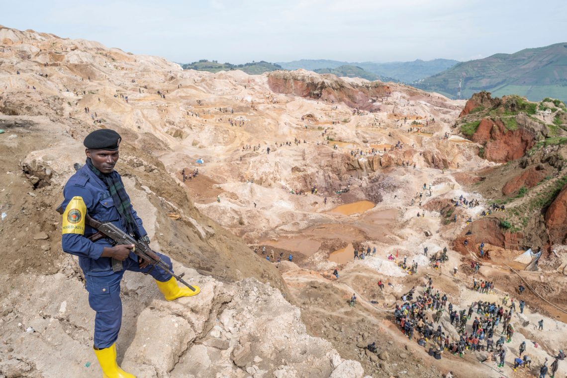 Ein bewaffneter Mann mit Baskenmütze steht am Rande einer Coltanmine. Unten sieht man Minenarbeiter. Das Bild ist Teil eines Beitrags über Entwicklungshilfe und die Frage, ob Afrika zuviel Hilfsgelder bekommt.
