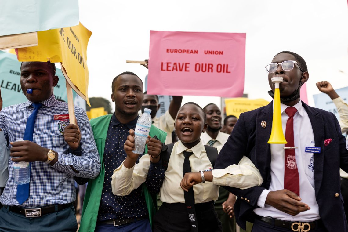 Junge Menschen mit Pfeifen gehen untergehakt eine Straße entlang. Sie tragen Schilder mit der Aufschrift European Union Leave Our Oil. Das Bild ist Teil eines Beitrags über Entwicklungshilfe.