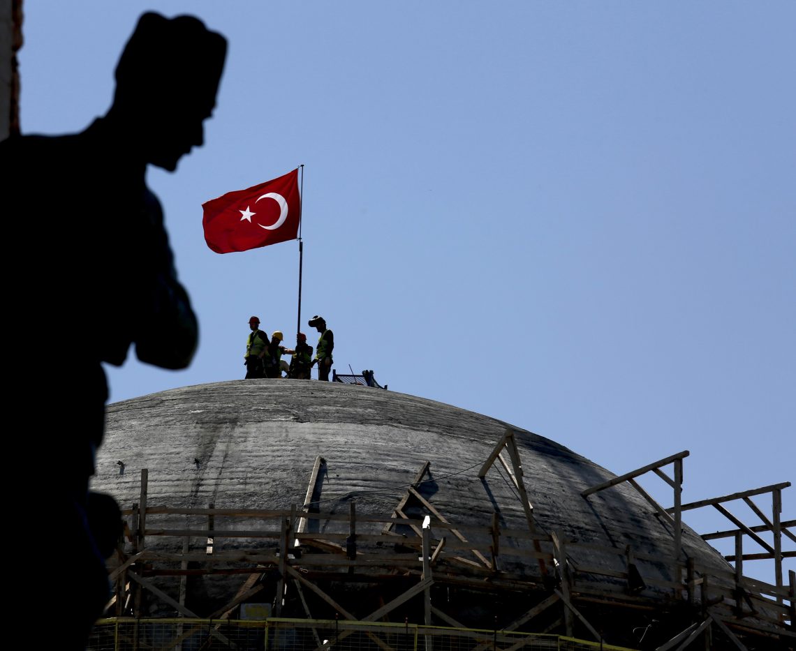 Taksimplatz in Istanbul: Im Vordergrund ist die Silhouette einer Statue des türkischen Staatsgründers Atatürk zu erkennen, im Hintergrund montieren Bauarbeiter eine türkische Flagge auf die im Bau befindliche Moschee.