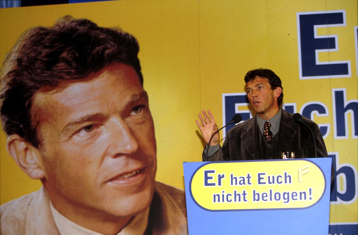 Archivbild von Jörg Haider aus dem Jahr 1995: der FPÖ-Politiker hält iene Wahlkampfrede vor einem Plakat mit seinem überdimensionierten Konterfei und vor einem Pult mit der Aufschrift „Er hat Euch nicht belogen“