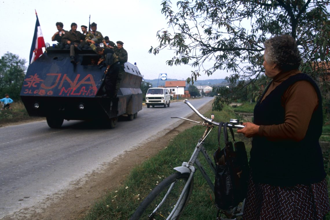 25. Juni 1991: Im kroatischen Pakrac beobachtet eine Frau einen Truppenpanzer der jugoslawischen Armee, die den Ort angreift.