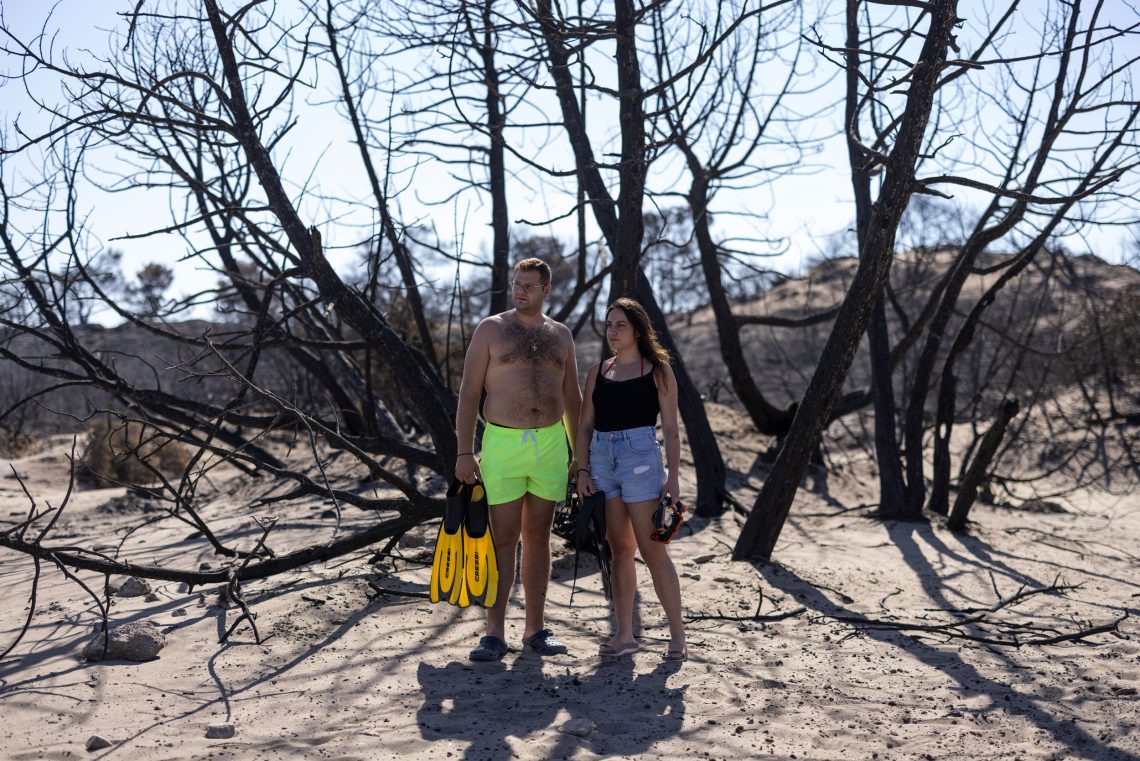 Zwei Menschen in Bade- bzw. Sommerbekleidung stehen unter einem verbrannten Strauch. Der Mann hält zwei Taucherflossen in der Hand. Beide scheinen auf das Meer zu blicken.