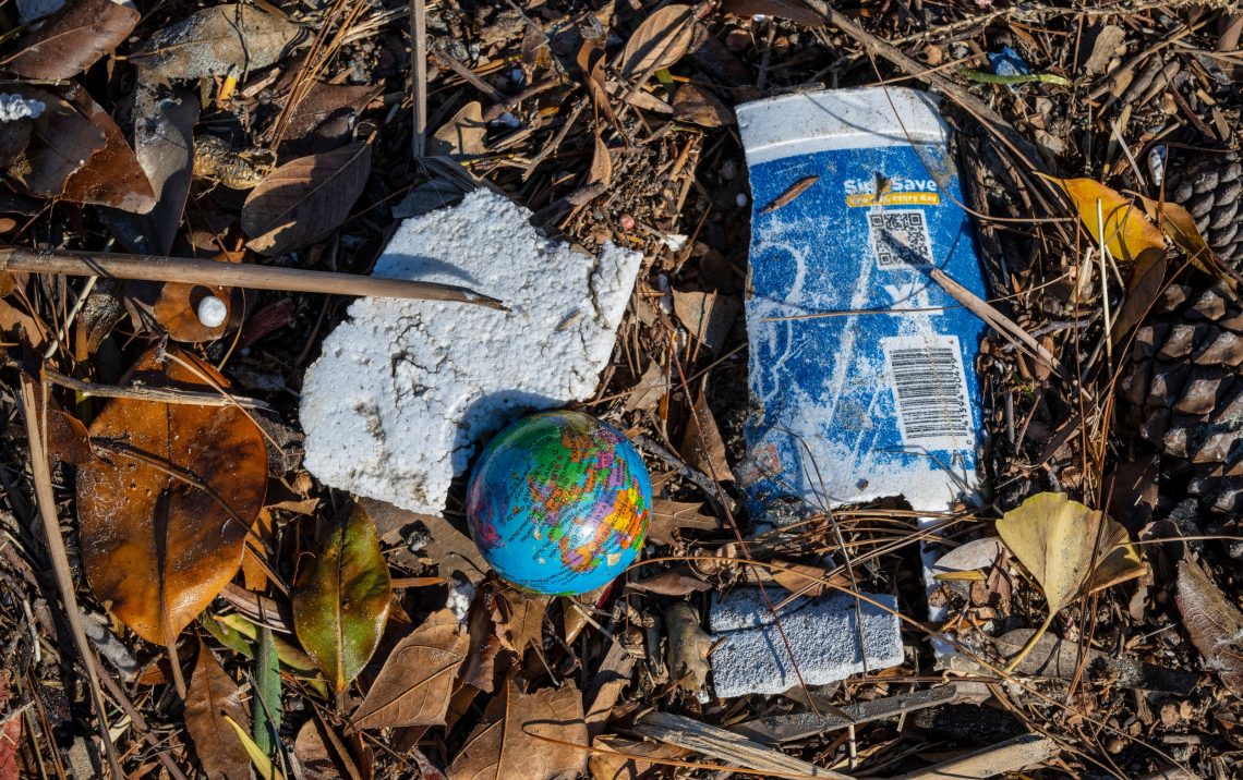 Plastikmüll auf einem Strand, darunter Styropor und eine Weltkugel aus Plastik sowie ein ausgeblichener Joghurtbecher. Das Bild illustriert einen Beitrag über Plastik im Meer und die Folgen.