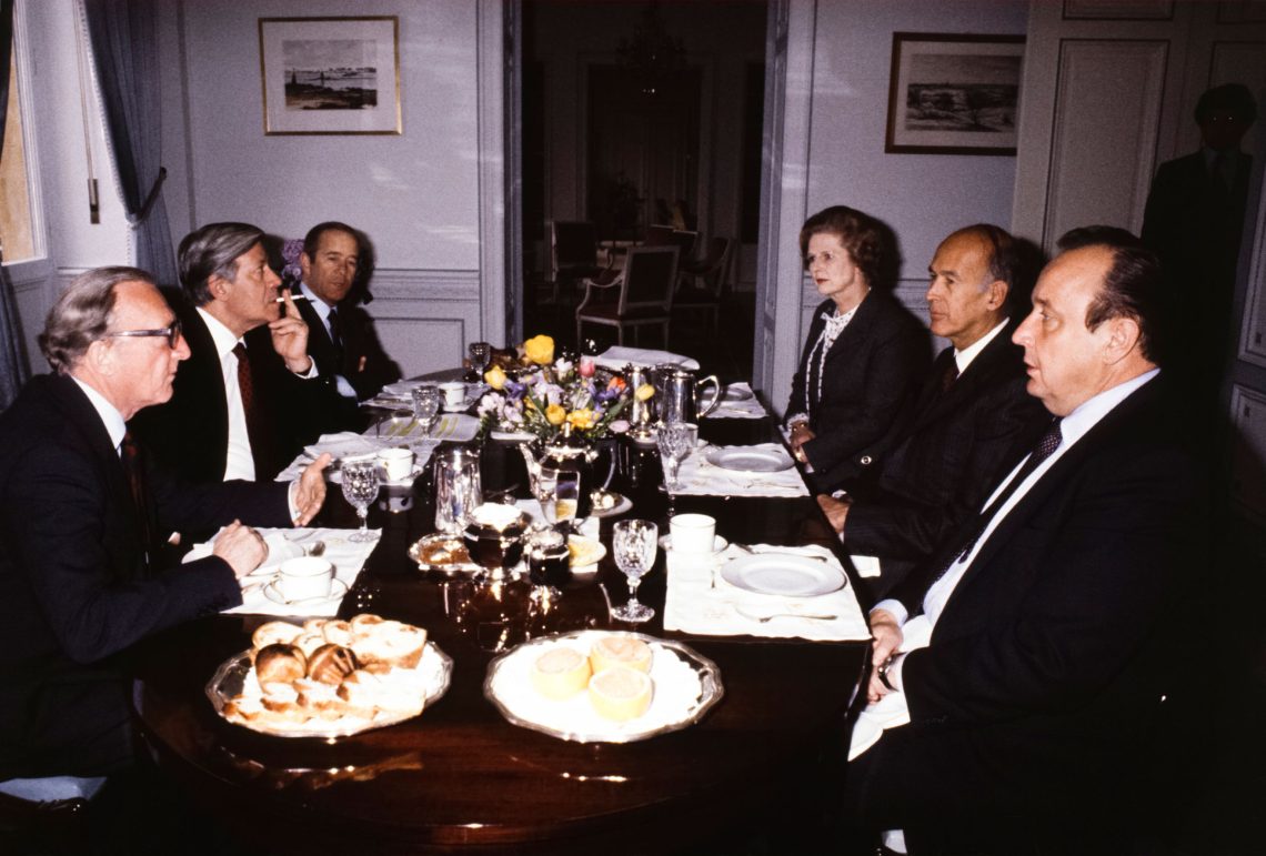 Eine Tischszene mit den Politikern der 1980er Jahre: Valéry Giscard d'Estaing, Helmut Schmidt, Lord Carrington, Jean François-Poncet, Margaret Thatcher und Hans-Dietrich Genscher bei einem Frühstück in einem hell-lila gestrichenen Raum in einem älteren Gebäude. Es stehen Blumen auf dem Tisch. Das Bild ist Teil eines Beitrags über Essen und Politik.