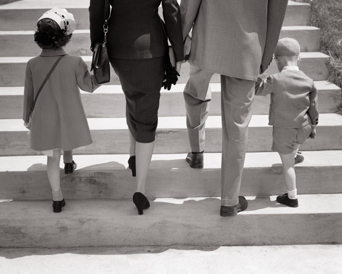 1940er 1950er: Rückansicht einer Familie, die gemeinsam die Treppe hinaufgeht und sich an den Händen hält, Mutter, Vater und Tochter und Sohn.