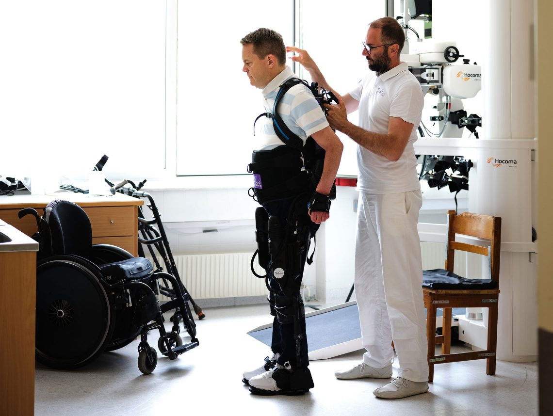 Ein Therapeut hilft einem querschnittgelähmten Patienten in ein Exoskelett.