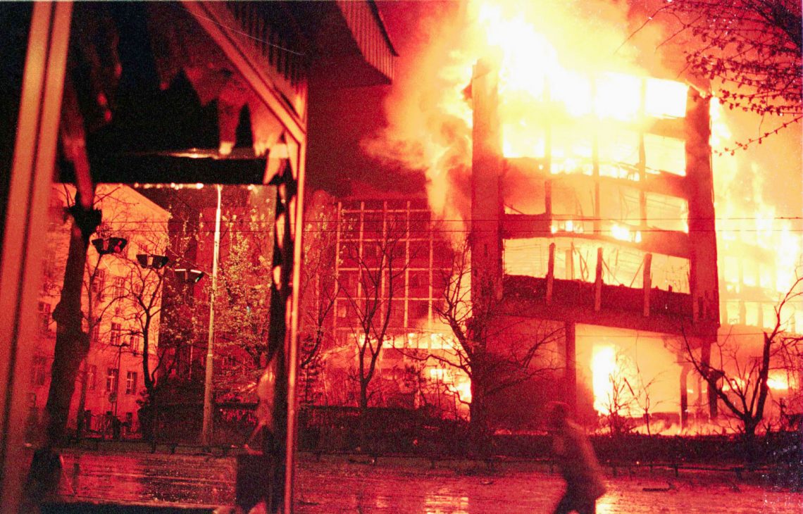 Ein Gebäude brennt in der Nacht. Es ist das Innenministerium in Belgrad im April 1999. Ein Mann im Vordergrund flüchtet vor dem Feuer.