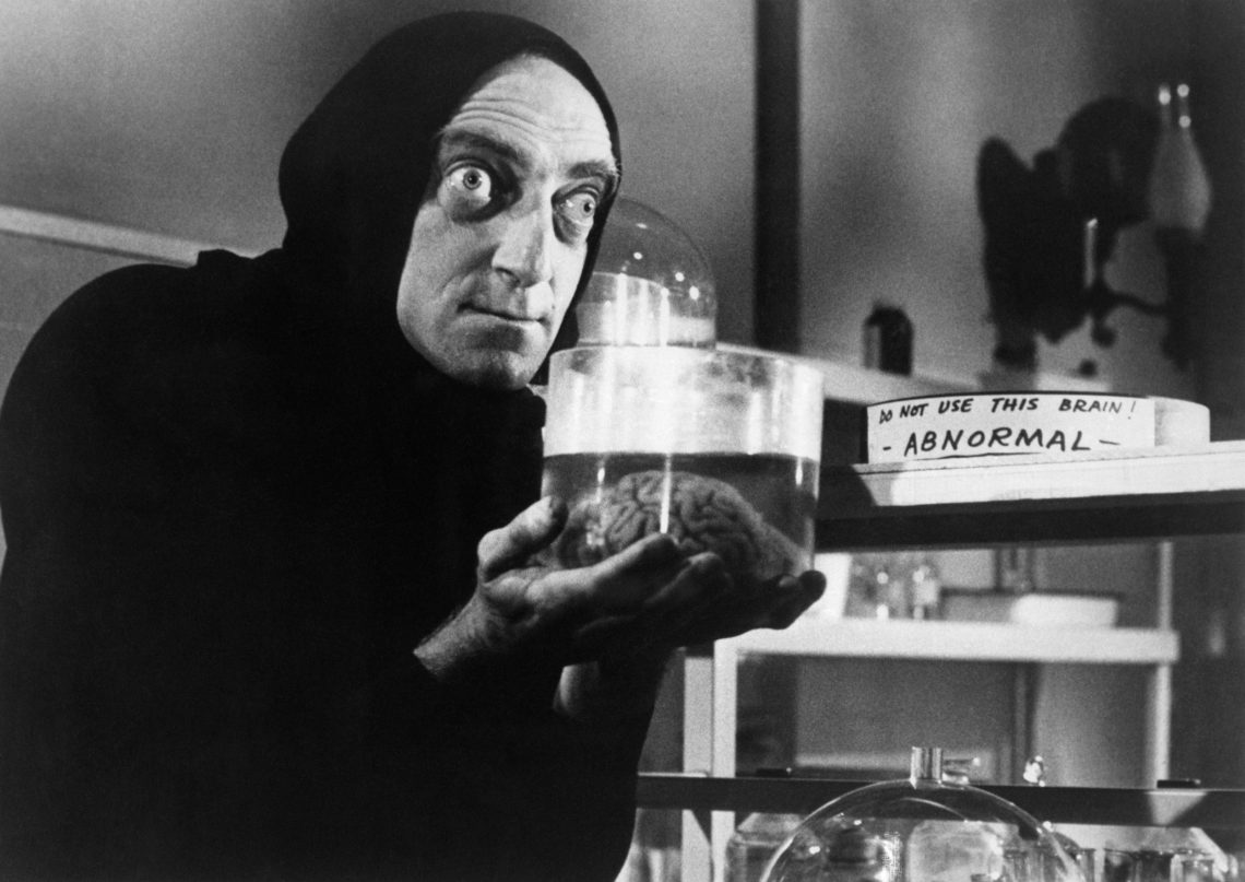 Marty Feldman als Igor in Young Frankenstein, der ein Gefäß mit einem Gehirn in den Händen hält. Das Bild ist Teil eines Beitrags über Transhumanismus.