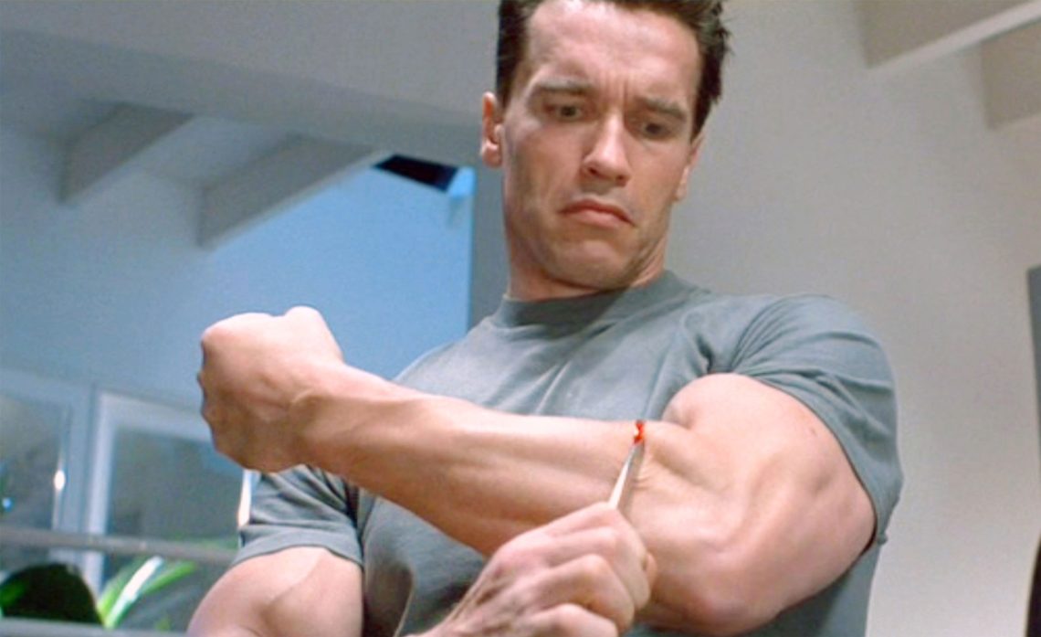 Arnold Schwarzenegger als Terminator in Terminator 2, Judgement Day. Er schneidet an seinem Unterarm das Gewebe auf, um seinen darunter liegenden echten Arm, ein Endoskelett aus Plastik und Stahl, freizulegen. Das Bild ist Teil eines Beitrags über die Frage, was transhuman ist.