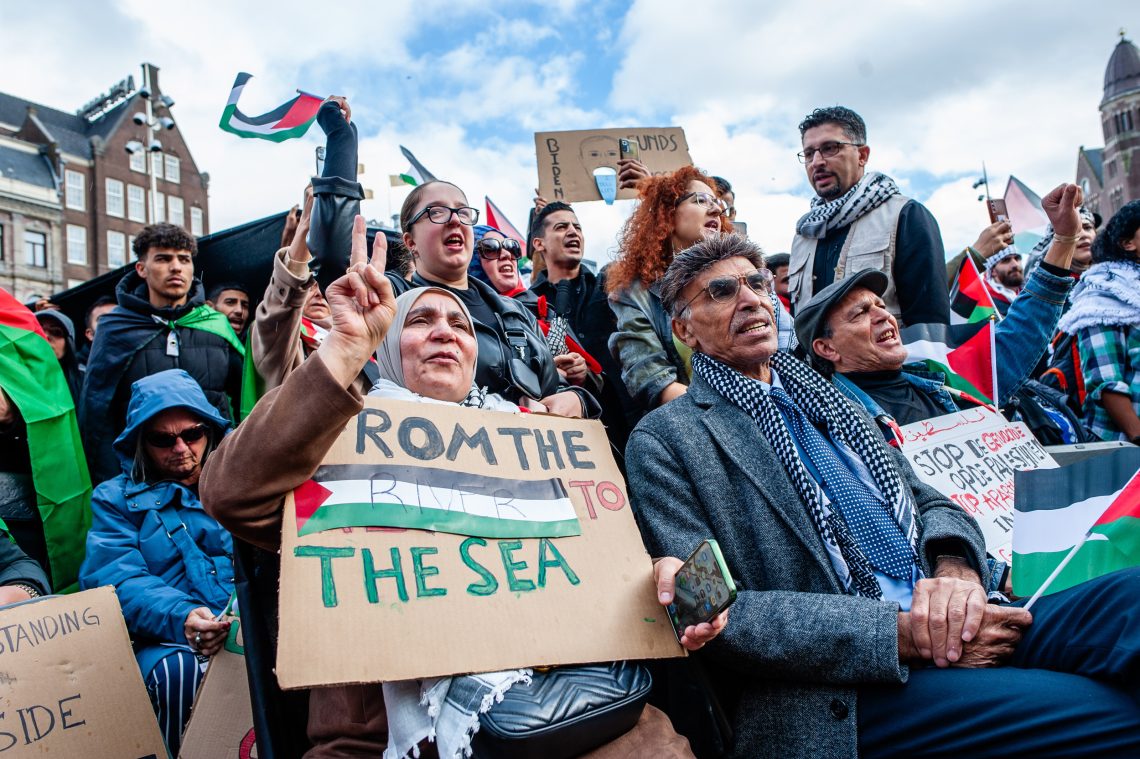 Pro-palästinensische Demonstration in Amsterdam am 15. Oktober 2023. Im Zentrum des Bildes ist eine Frau, die ein Schild mit der Aufschrift „From the river to the sea“ (dt.: Vom Fluss bis zum Meer) hält. Das Bild illustriert einen Kommentar zum Überfall der Hamas auf Israel.