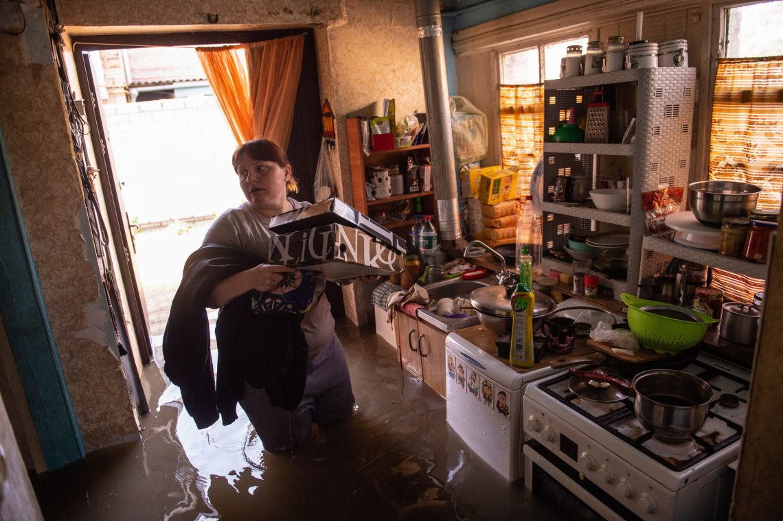 Eine Frau watet in kniehohem Wasser in ihrer Wohnung, um noch Gegenstände zu retten.
