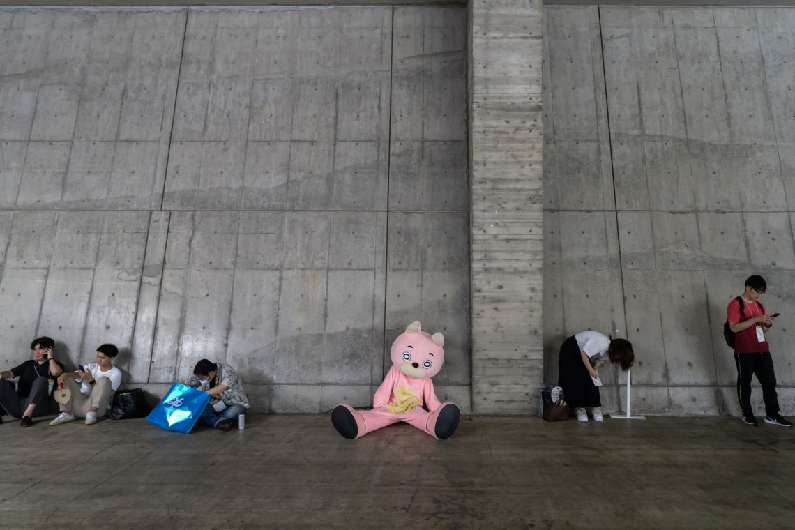 Ein Mensch in einem rosa Plüschkostüm, das eine Figur aus einem Computerspiel darstellt, sitzt auf dem Boden an eine Betonwand gelehnt. Das Bild illustriert einen Beitrag, in dem es um Technik und Natur geht.