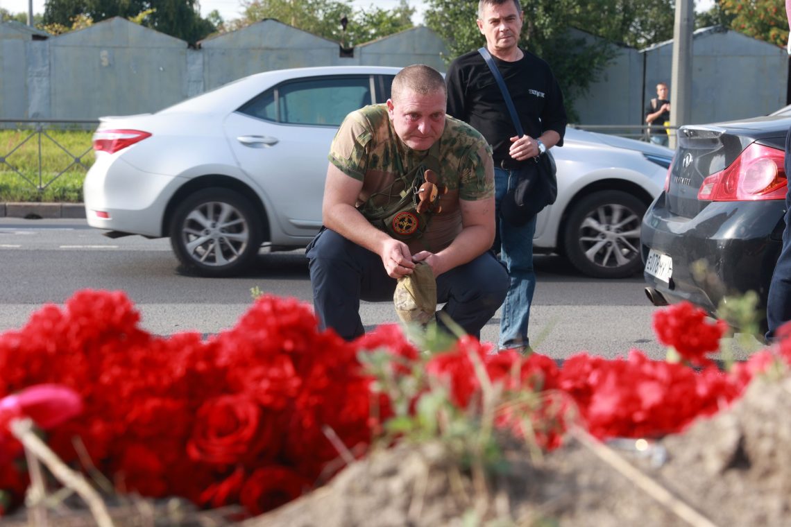 Ein Mann hockt mit Tränen in den Augen vor roten Rosen und hält eine grüne Kappe in der Hand.