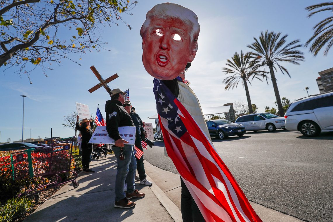 Anhänger von Donald Trump stehen auf einer Straße und halten sein Konterfei, die amerikanische Flagge und Kreuze in die Luft.