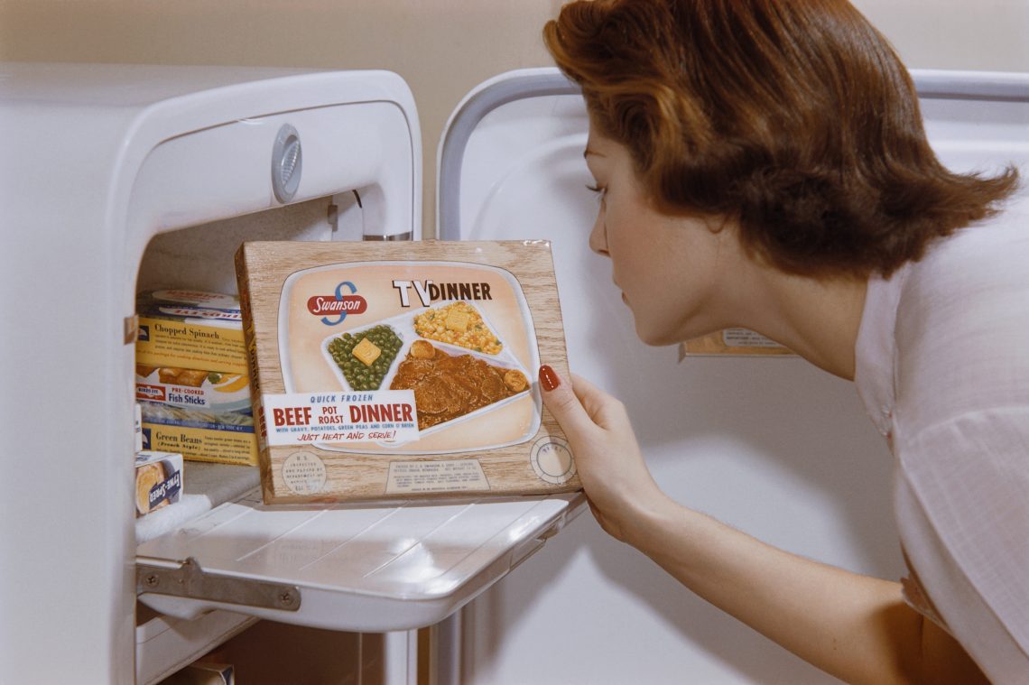 Eine Frau betrachtet ein Fertiggericht, das sie aus dem Gefrierschrank genommen hat. Das Bild illustriert einen Artikel zum Thema ultra-verarbeitete Lebensmittel.