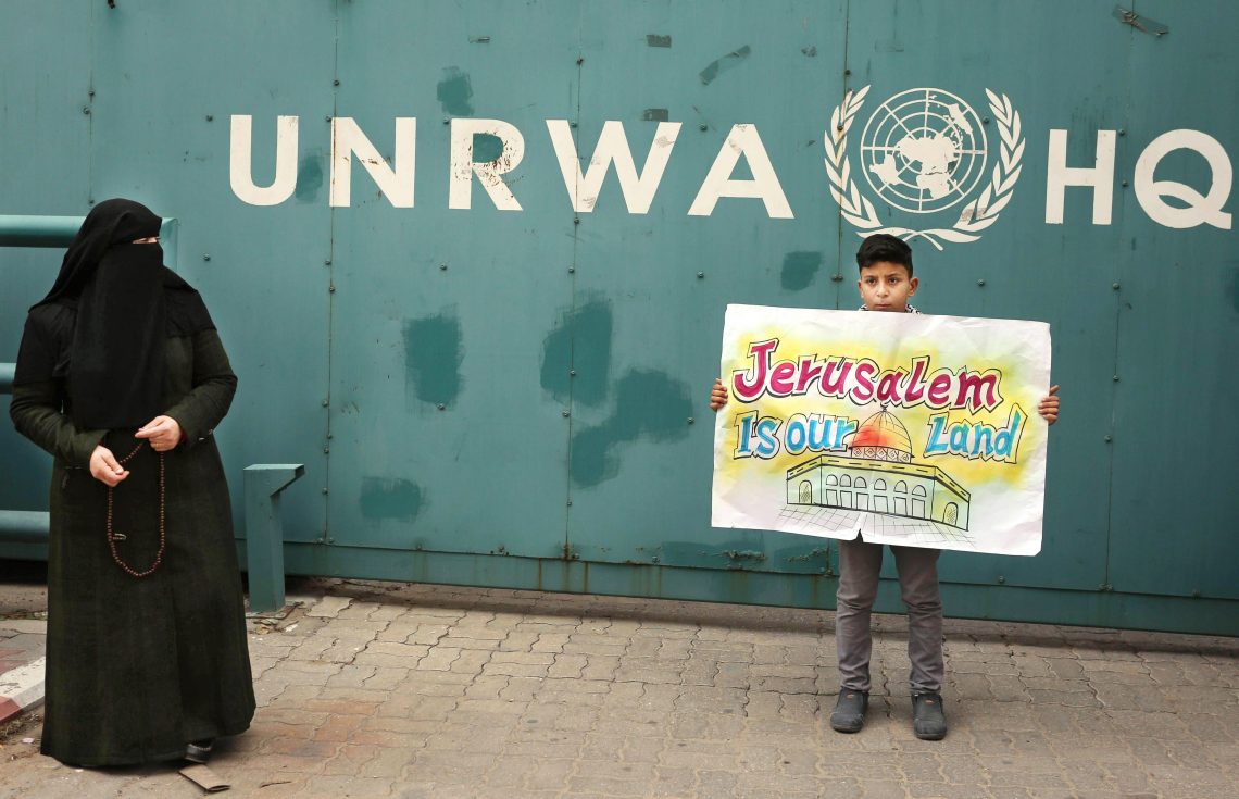 Ein Kind hält ein Schild mit der Aufschrift „Jerusalem is our Land“ in den Händen vor dem Headquarter der UNRWA in Gaza. Das Bild illustriert einen Artikel über das Flüchtlingshilfswerk UNRWA.