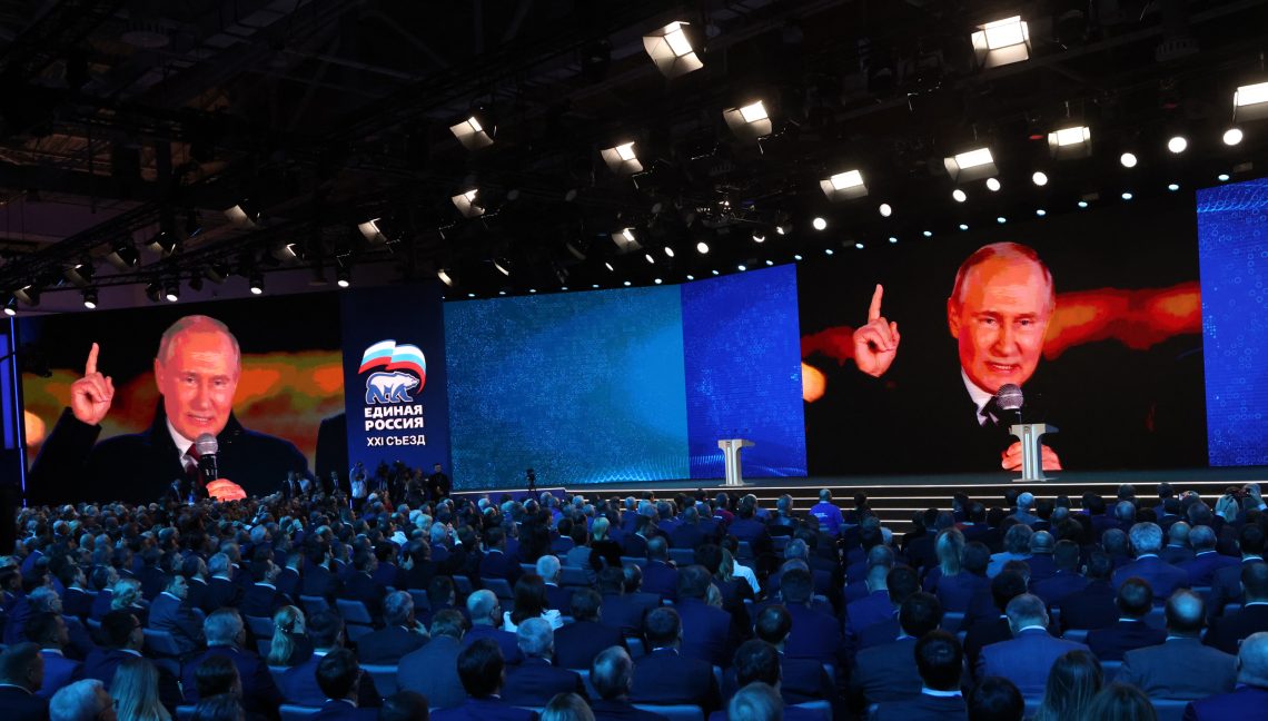 Wladimir Putin auf einer Leinwand während des 21. Kongresses seiner Partei „Einiges Russland“ am 17. Dezember 2023 in Moskau. Im Vordergrund ist Publikum zu sehen. Das Bild illustriert einen Artikel zu den Präsidentschaftswahlen in Russland.