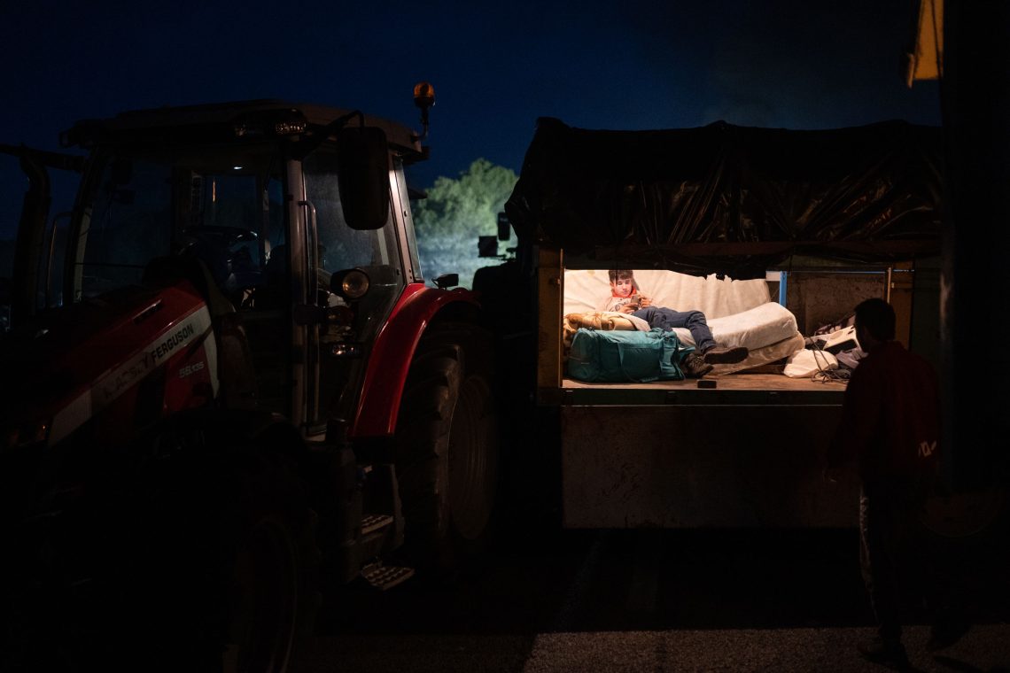 Blick in einen Anhänger am Abend der Proteste der spanischen Bauern auf der A7. Ein Junge sitzt auf einem provisorischen Bett und liest etwas auf seinem Handy.