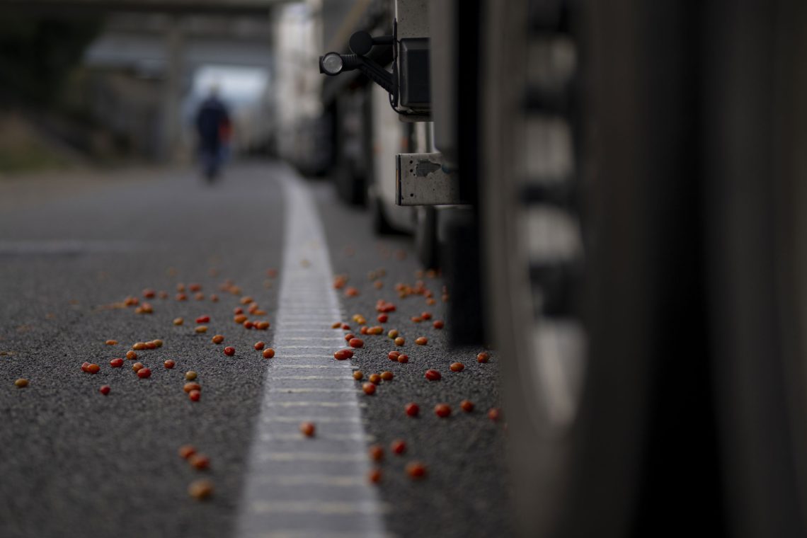 Tomaten liegen neben einer LKW-Schlange auf der Straße. Das Bild illustriert ein Interview über Landwirtschaft.