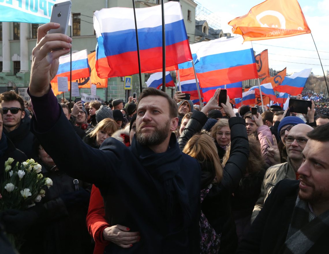 Ein Demonstrationszug mit orangen und russischen Fahnen. Im Vordergrund steht Alexej Nawalny.