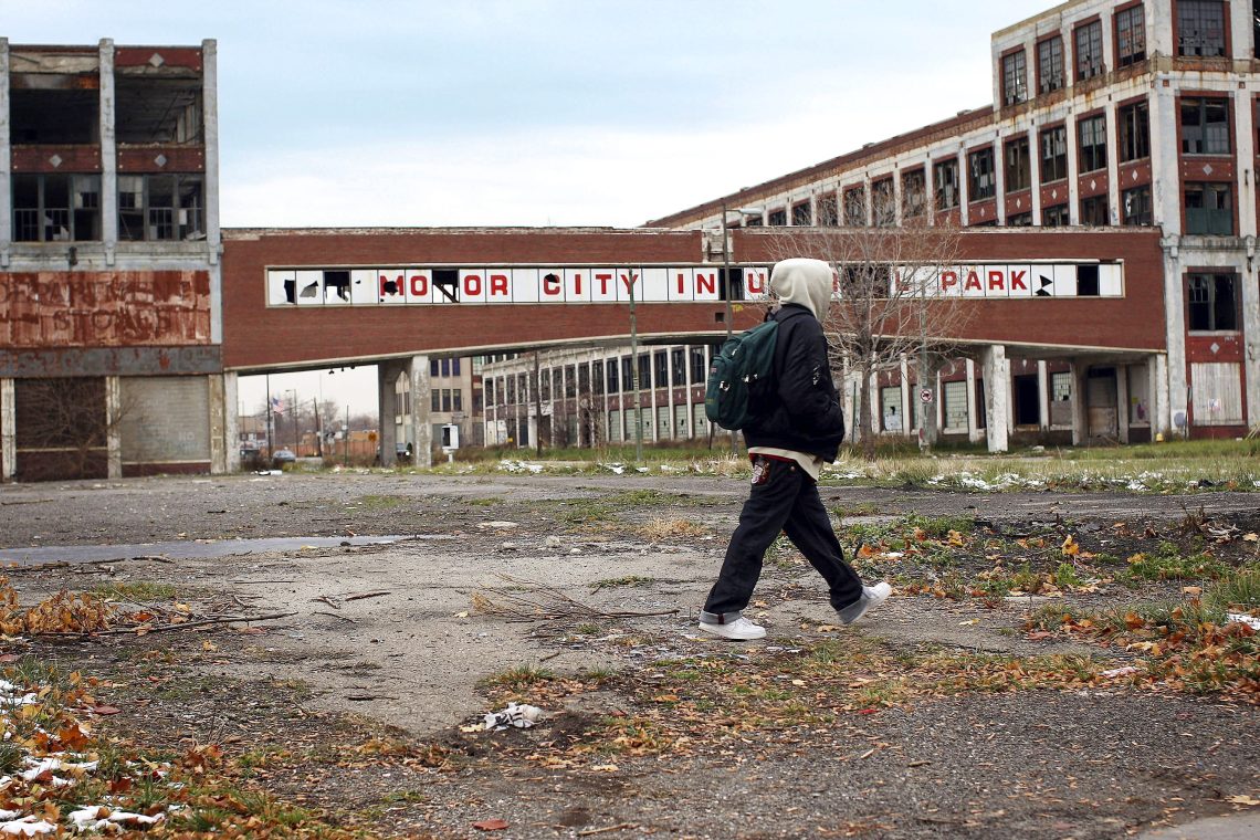 Das Bild zeigt eine verlassene und zerfallene Automobilfabrik, an der ein Jugendlicher vorbeigeht. Das Bild illustriert einen Artikel über das Verbrenner-Verbot in Europa.