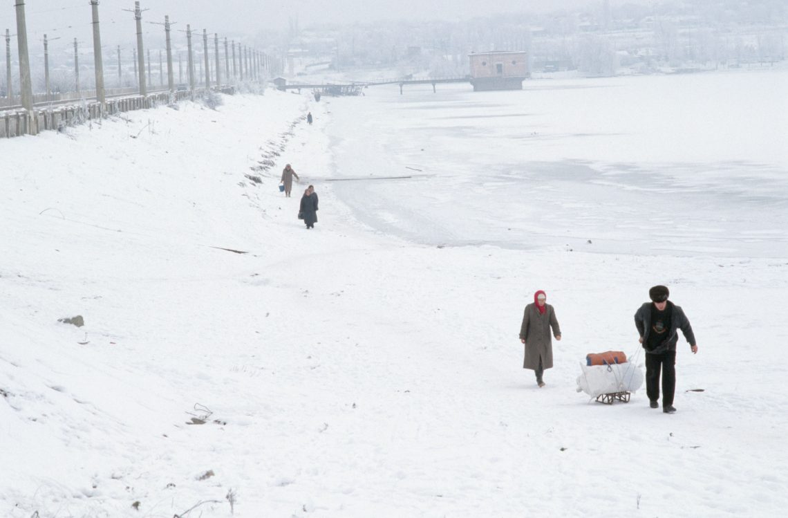 Aufnahme einer Stadt und eines zugefrorenen Gewässers im Schnee. Mehrere Menschen gehen im Schnee und ziehen ihren Besitz auf einem Schlitten hinter sich her. Das Bild ist Teil eines Beitrags über Russland und die Ukraine.