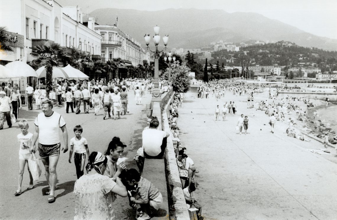 Eine belebte Promenade in Jalta am Schwarzen Meer. Viele Menschen gehen in Sommerkleidung, blicken auf das Meer und essen Eis.