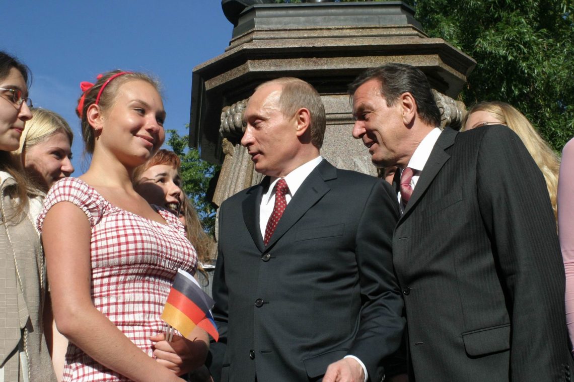 Foto von Wladimir Putin und Gerhard Schröder, die ein blondes junges Mädchen mit einer Deutschlandflagge in der Hand anstarren. Das Bild illustriert einen Beitrag über die Ukraine.
