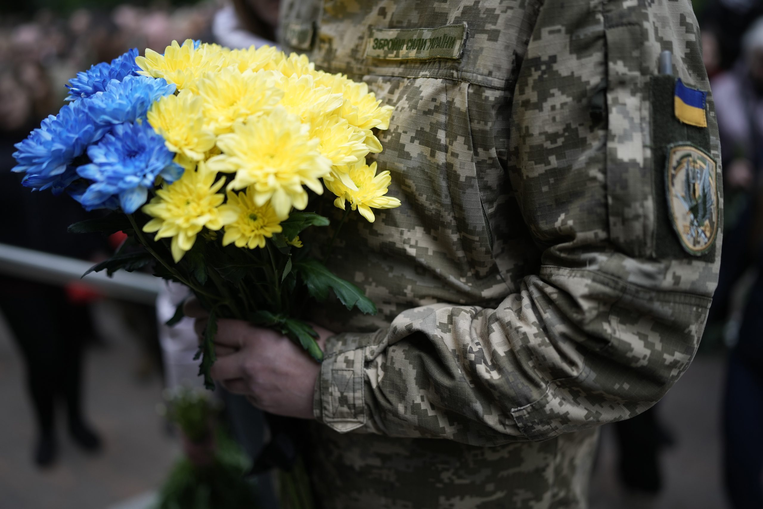 Ein ukrainischer Soldat hält einen Blumenstrauß mit gelben und blauen Blumen in den Händen. Das Bild illustriert den Kommentar über die Angst vor dem Sieg im Ukrainekrieg.