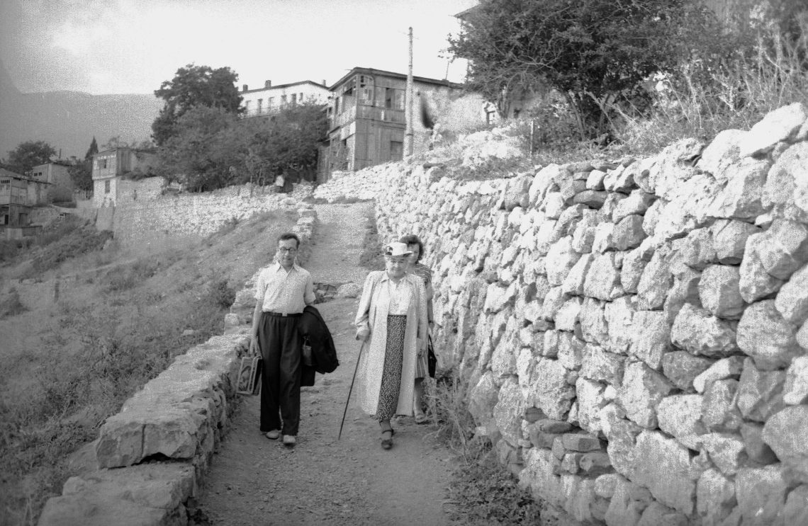 Olga Knipper-Tschechowa auf einem Spaziergang mit zwei weiteren Personen in einer mediterran anmutenden Landschaft. Das Foto wurde 1949 auf der Krym aufgenommen.