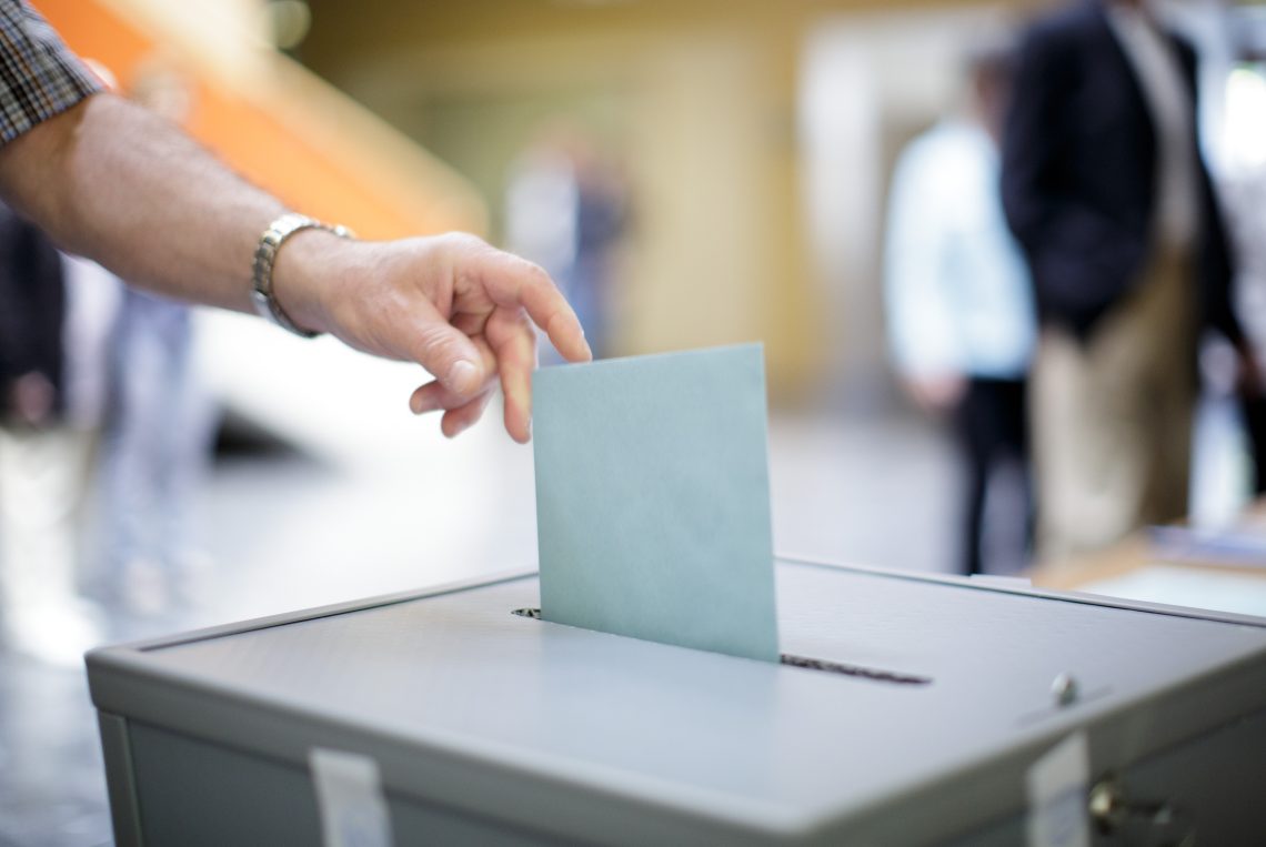 Ein Mann wirft seinen Stimmzettel in die Wahlurne bei der Präsidentschaftswahl in Österreich 2016. Das Bild illustriert einen Kommentar über die anstehenden Wahlen.