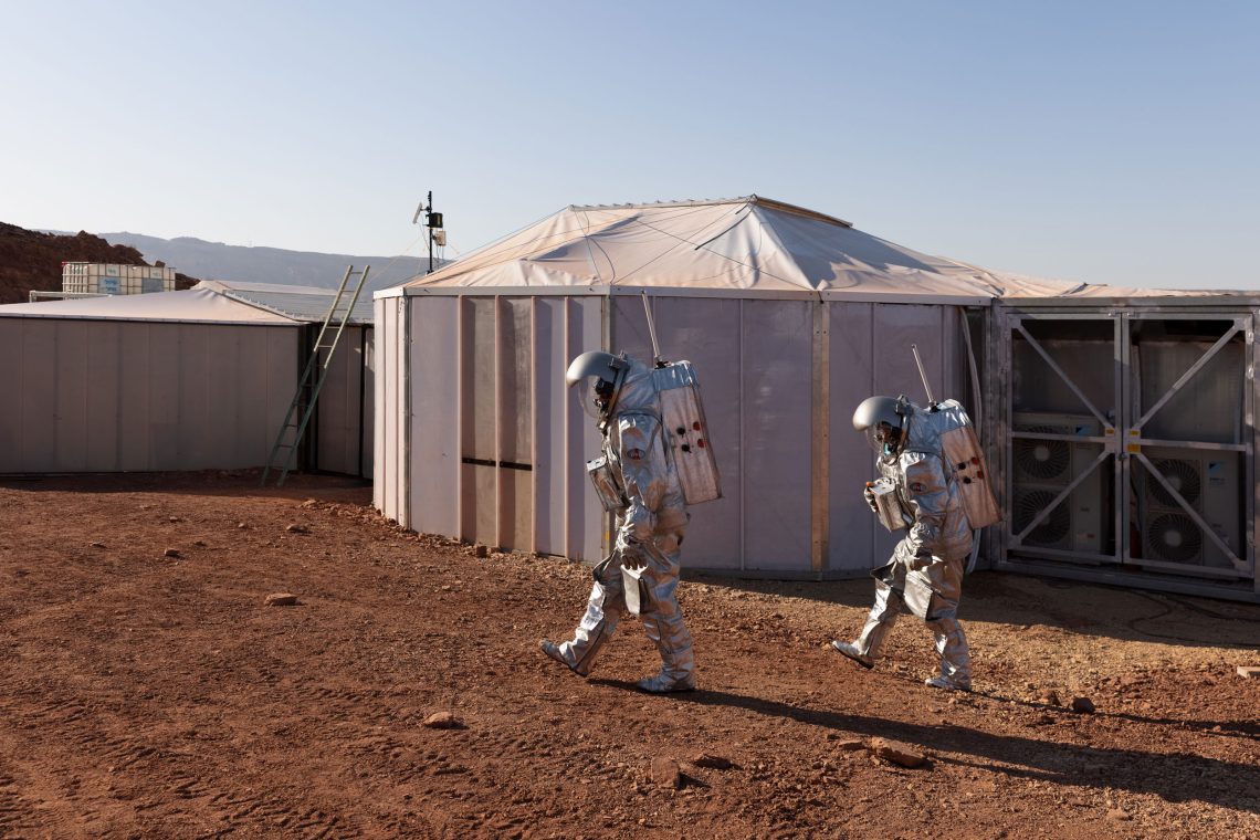 Menschen in Raumanzügen gehen in einer marsähnlichen Landschaft an einer Art Raumstation vorbei. Das Bild ist Teil eines Beitrags, in dem es um die Besiedlung des Mars geht.
