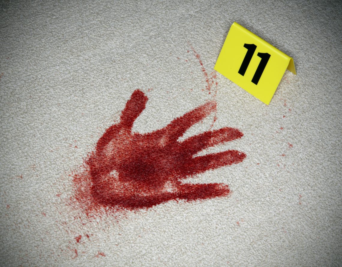 Das Bild zeigt einen blutigen Handabdruck auf einen Teppich. Daneben ist ein gelber Aufsteller mit der Zahl 11 zu sehen, der der Spurensicherung dient. Das Bild illustriert ein Dossier zum Thema Forensik.