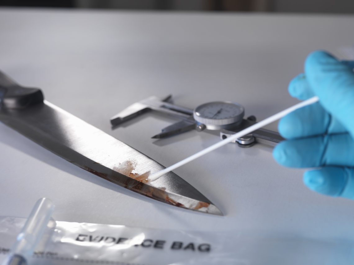 Das Bild zeigt eine blutige Schere, die mit einem Wattestäbchen auf DNA-Spuren untersucht wird. Das Bild illustriert einen Artikel über DNA-Analyse-Methoden und deren Genauigkeit.