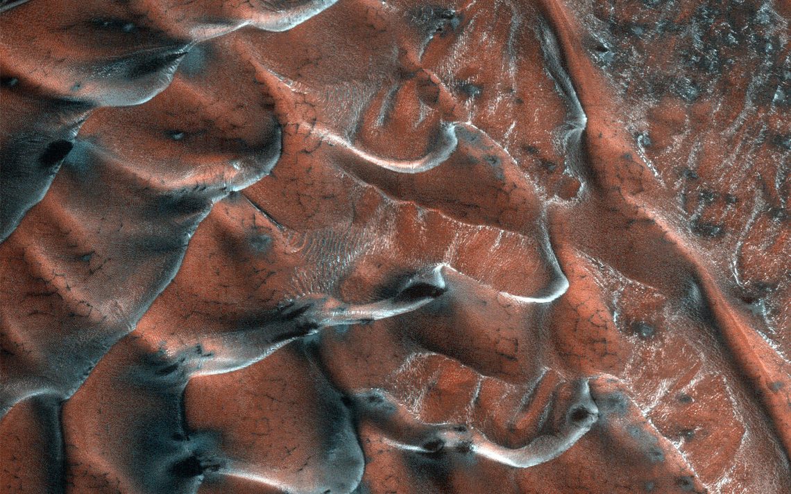 Die frostigen Sanddünen des Mars, aufgenommen am 22. März 2021 von der NASA. Die Dünen haben eine braunrote Farbe, schwarze Flecken und weiße Streifen. Farben und Strukturen erinnern an die schuppige Haut eines Reptils. Die Dünen befinden sich am Rand eines fünf Kilometer tiefen Kraters in den nördlichen Ebenen; ihre Struktur zeigt den Wissenschaftlern, dass es in diesem Bereich jahreszeitlichen Frost gibt.
