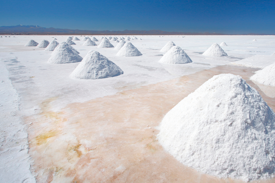 Dutzende Salzhaufen verteilen sich über die glatte, weiße Fläche der Salar de Uyuni in Bolivien. Das Bild illustriert einen Beitrag über die Rolle von Salz für die Wirtschaft.