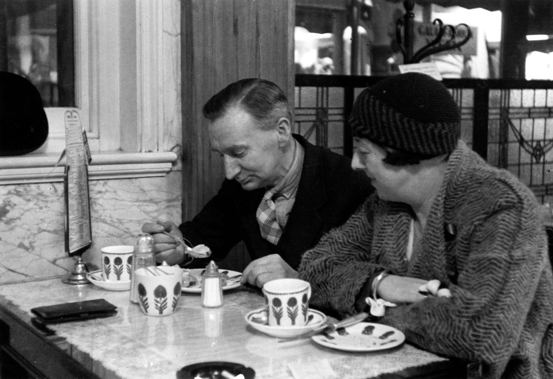 Ejn Paar sitzt an einem Tisch, der mit Kaffee- bzzw. Teegeschirr gedeckt ist. Der Mann isst gerade einen Kuchen während die Frau ihm zuschaut. Das Bild ist Teil eines Beitrags mit einem Podcast über die Geschichte des Essens.