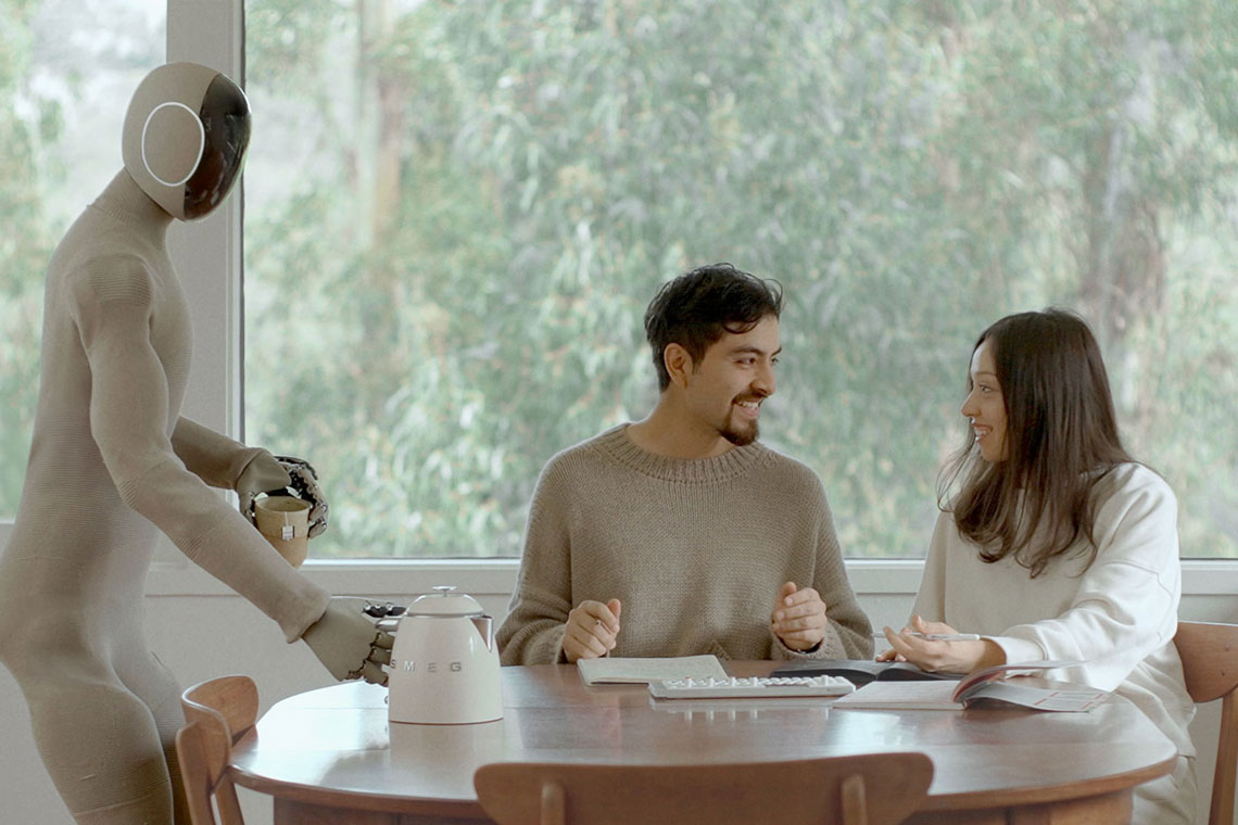 Kein Chatbot, sondern ein humanoider Roboter ist hier zu sehen: Er serviert Tee für ein Paar, das an einem Küchentisch sitzt.