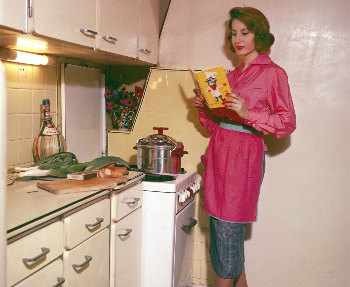 Eine Hausfrau in ihrer Küche Amenagee konsultiert sein Kochbuch, das er 1961 mit ihrem Schnellkochtopf geschrieben hat. Das Bild illustriert einen Artikel über die Geschichte von Kochbüchern.